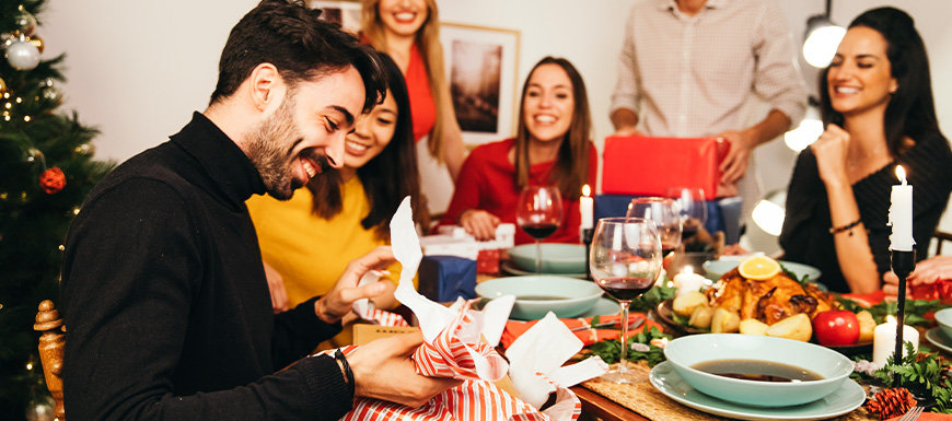 Man opening gift at dinner party with friends.